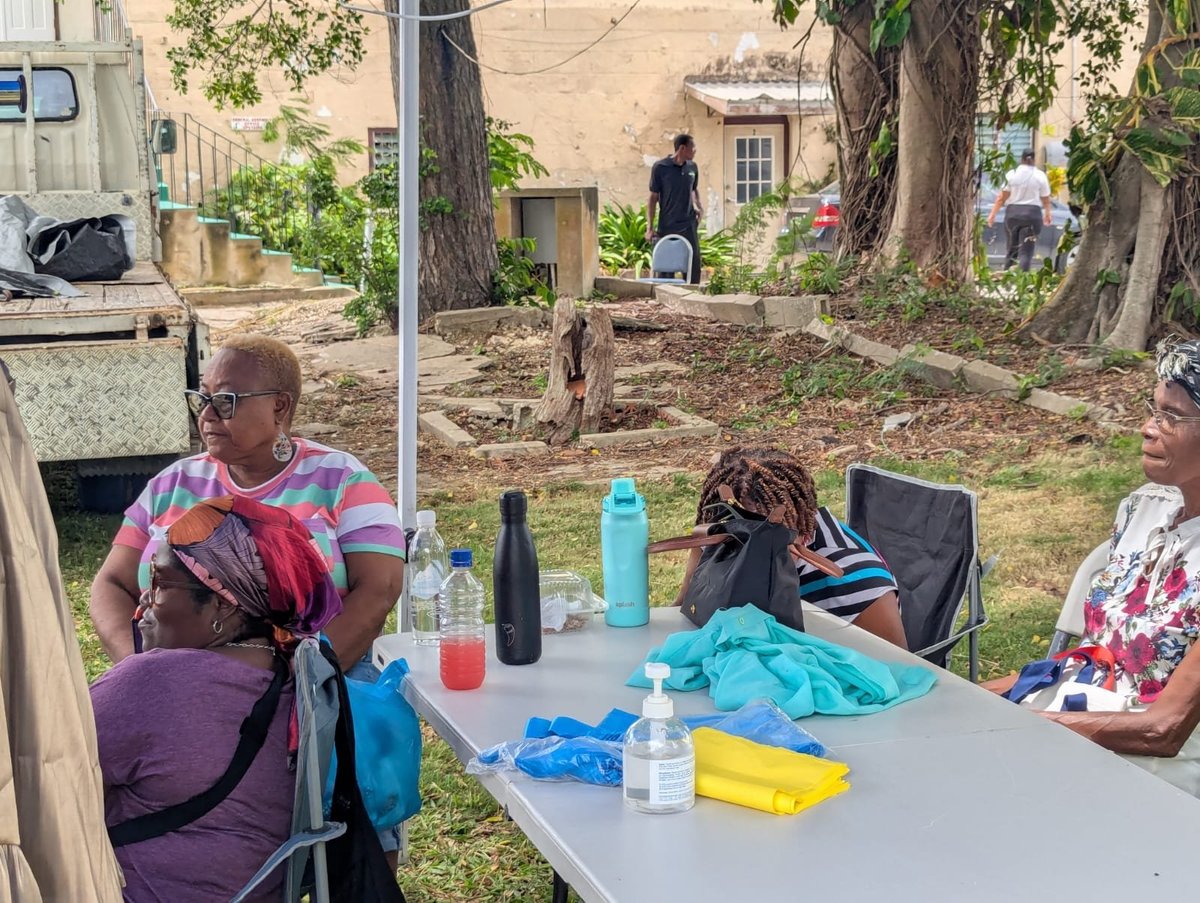 Group of people gathered outdoors around a table in a residential yard with trees and buildings visible in the background
