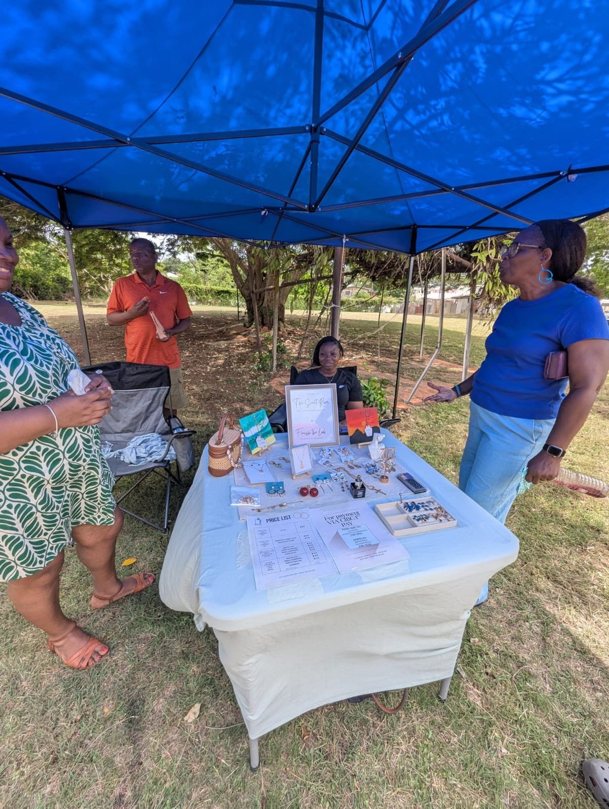 Community event under a blue tent canopy with people gathered around a white table displaying informational materials and crafts