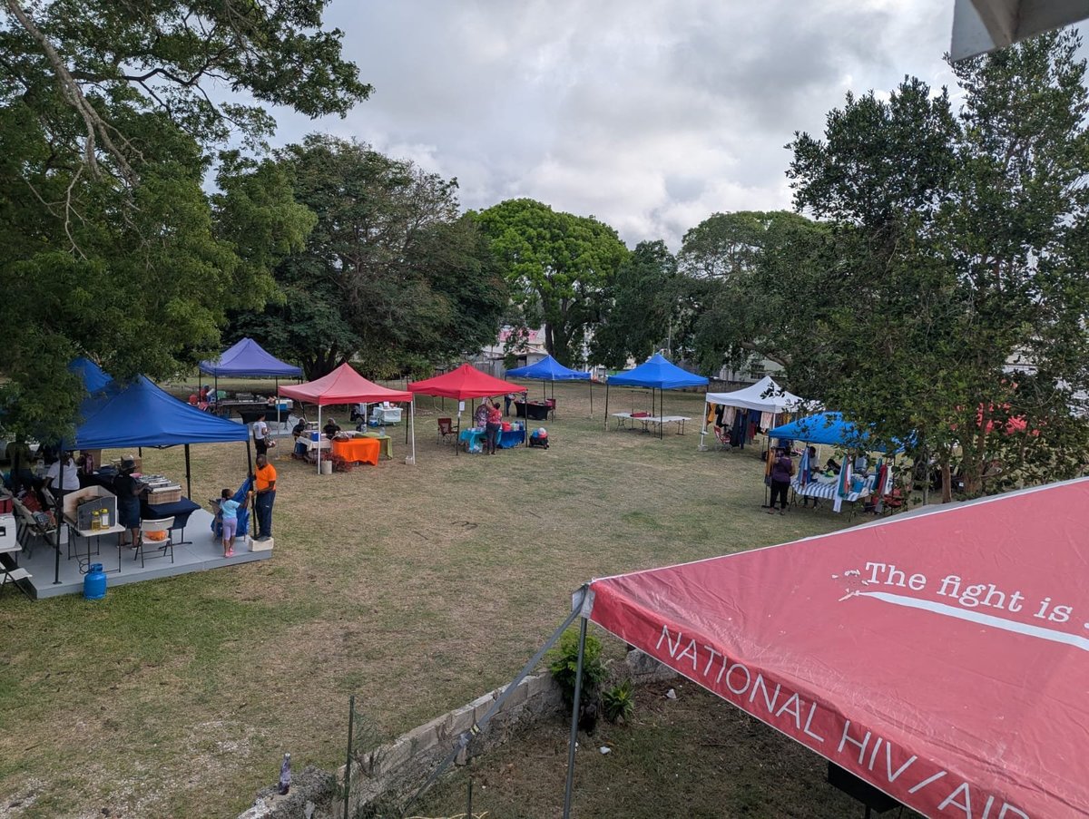 Wide angle of the outdoor flea market with blue and red canopy tents in a grassy field, with a National HIV/AIDS banner visible