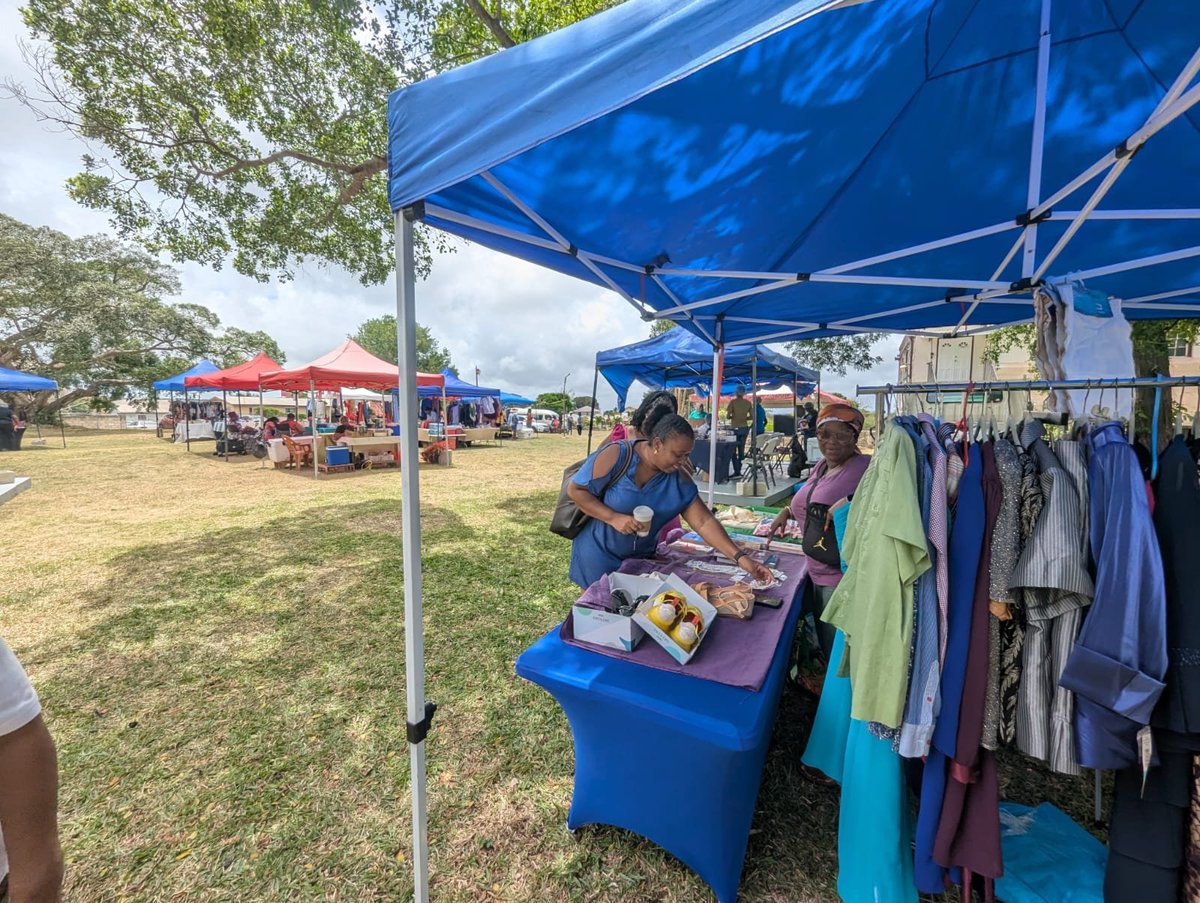 Outdoor market vendor under a blue tent selling clothing and goods from a table