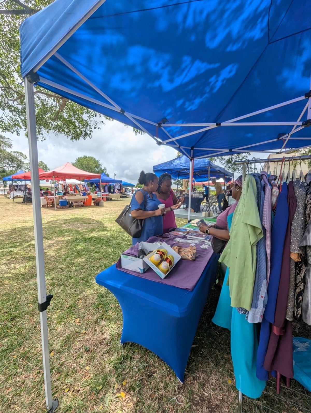Outdoor market vendor under a blue canopy tent selling clothing and food items at the community fair