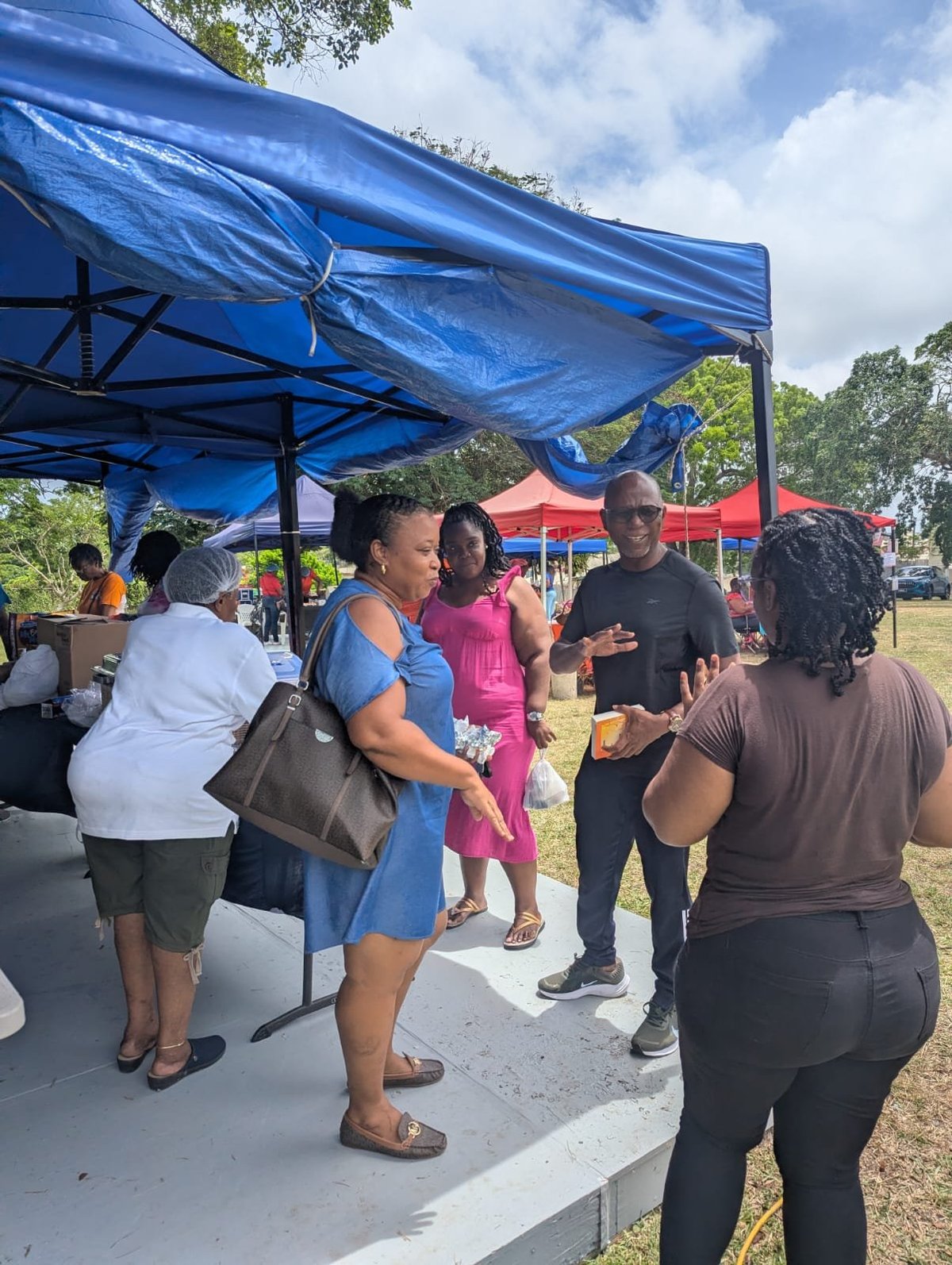 Group of people gathered under a blue tent at the outdoor community event, with red tents visible in the background